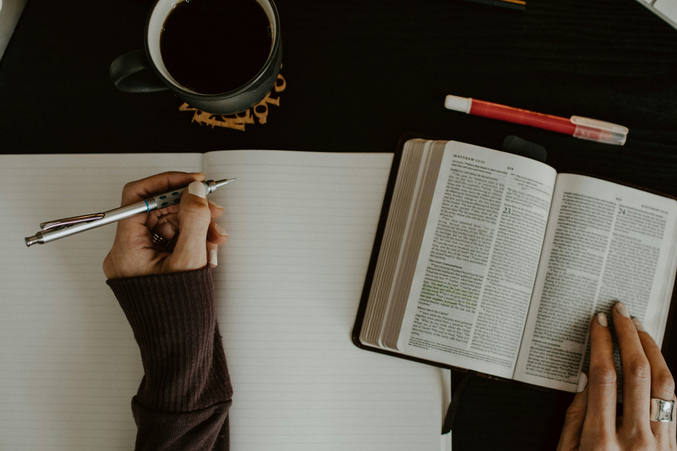 Person with Bible opened on table with pen and cup of coffee