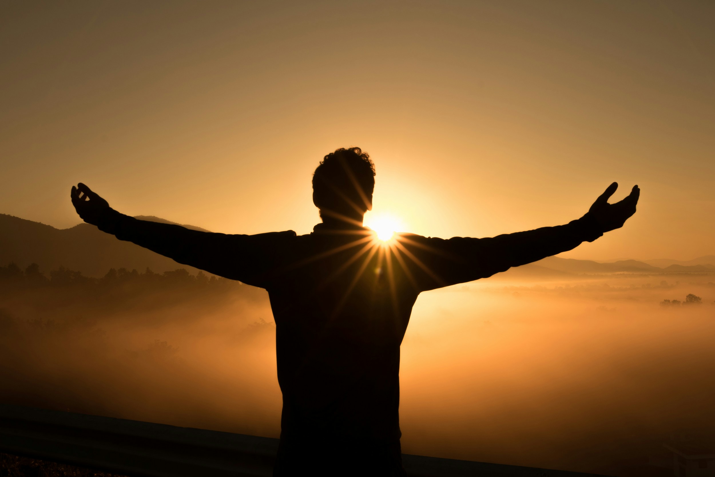 person standing at sunset with arms out.